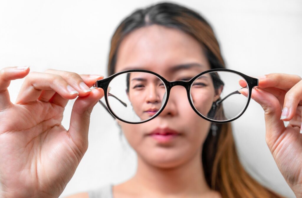 A squinting young woman holds a pair of eyeglasses up to the camera. Only her hands and glasses are in focus.