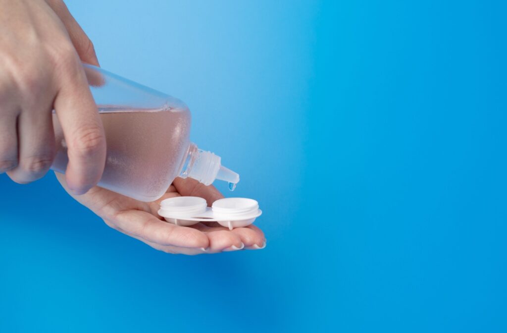 Against a blue background, a contact lens user drips cleaning solution into their contact lenses to clean them.