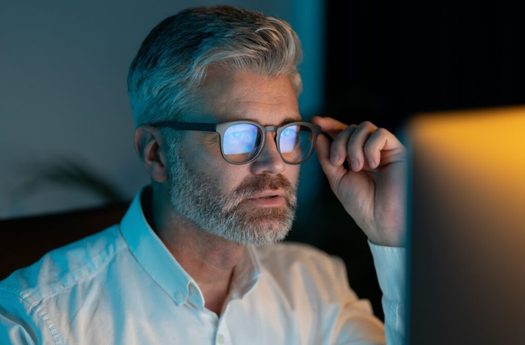 A person wearing glasses blue light stares at a computer screen in a dark room.