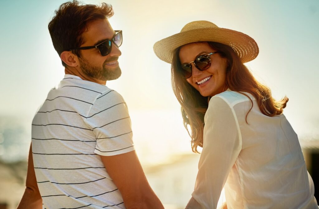 A smiling couple wearing sunglasses outdoors, while enjoying the sunny weather.