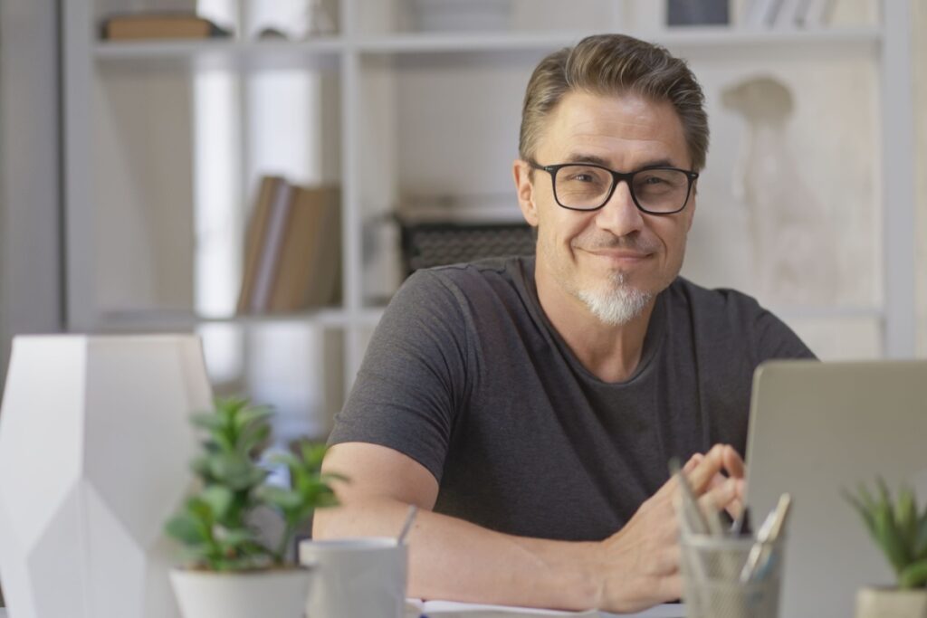 A person sitting a desk in front of a laptop, wearing glasses with anti-reflective coating.