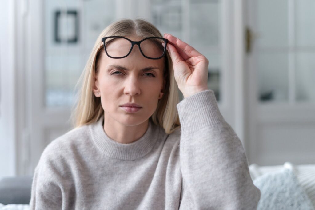 Woman holding up her glasses while squinting