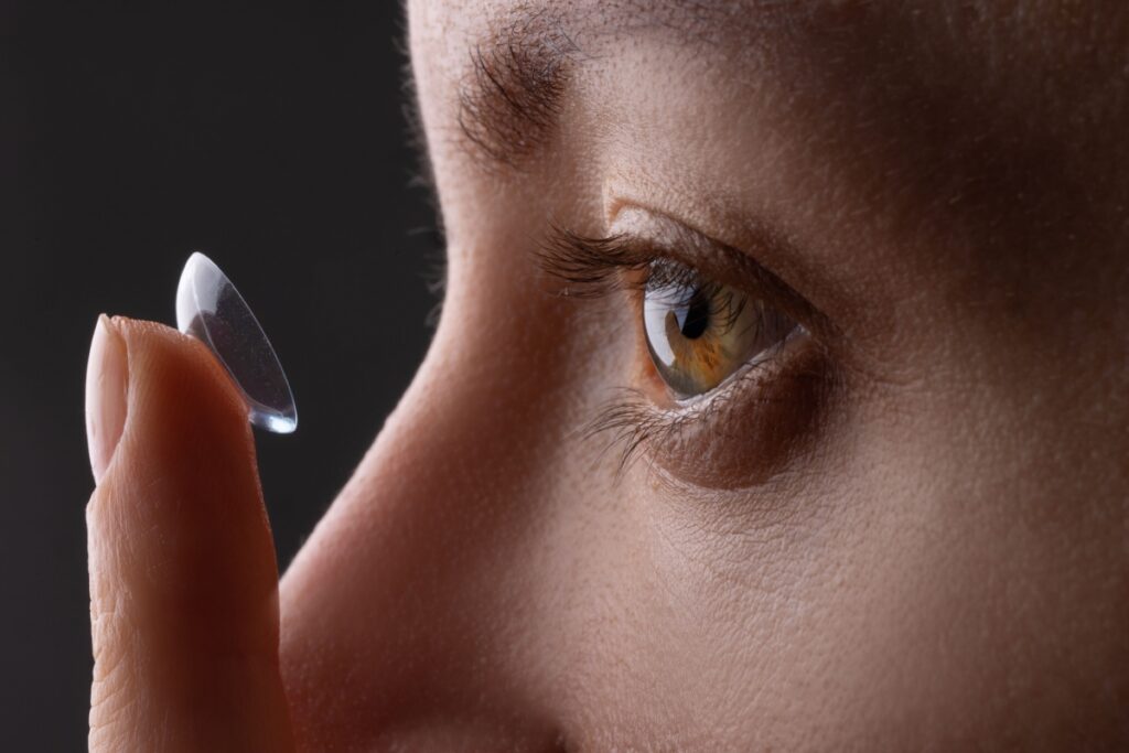 Woman putting holding up contact lens to left eye